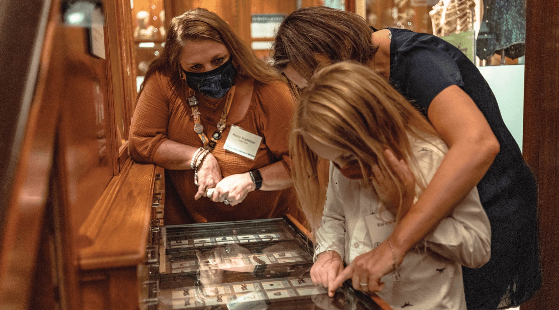 Two women and a young girl hovered over trays of small objects within the Museum gallery