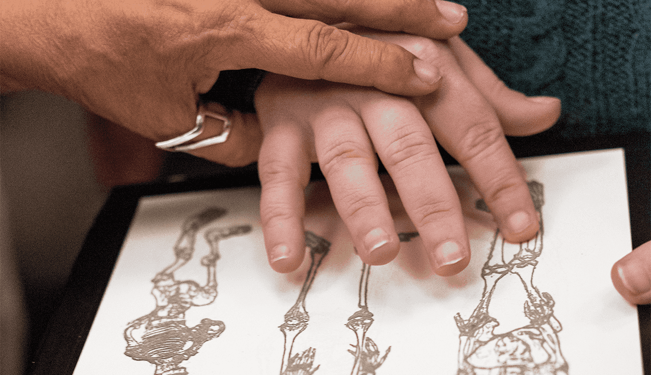 One hand guides another hand over a raised line drawing of skeletal illustrations