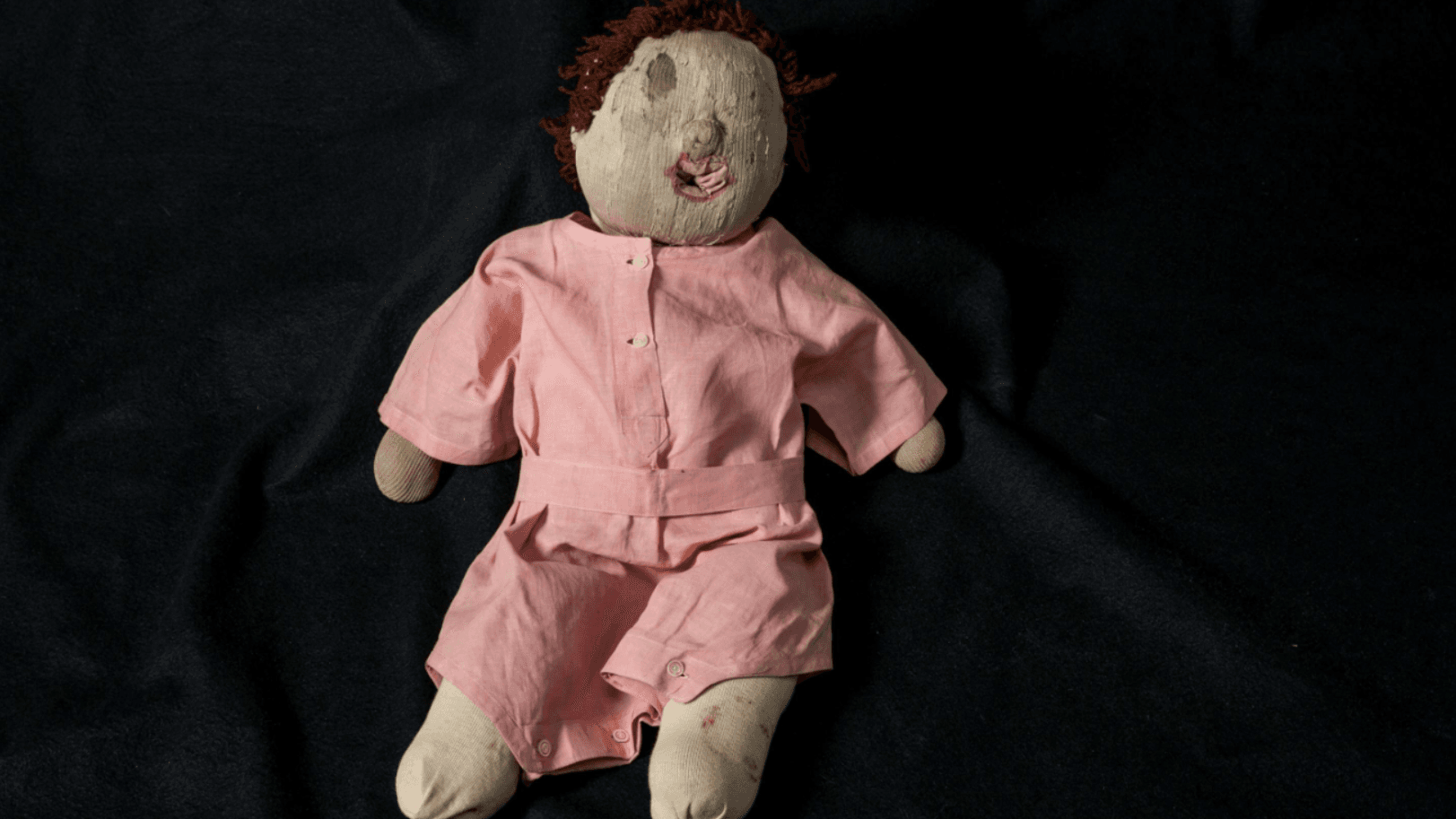 A photograph of a raggedy doll with no eyes in a pink dress
