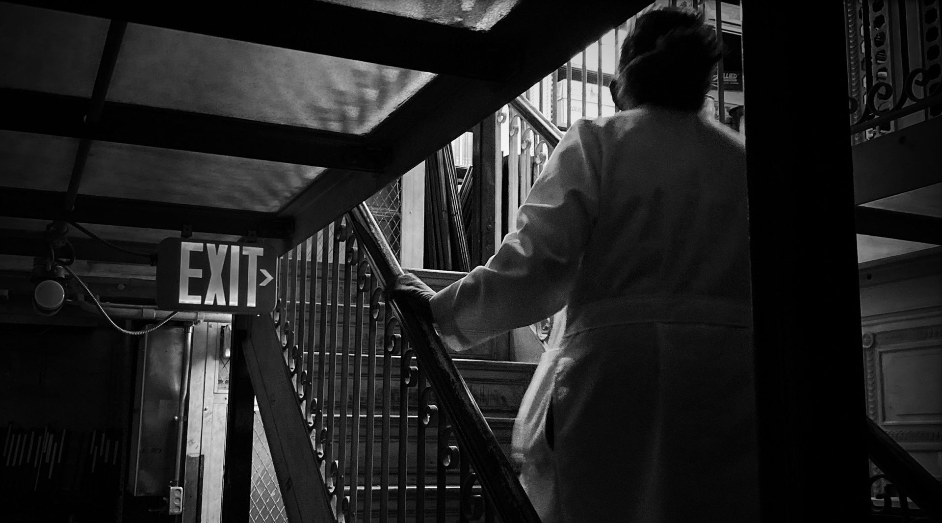 Black and white photograph of a woman in a lab coat ascending an iron staircase in a dimly lit space