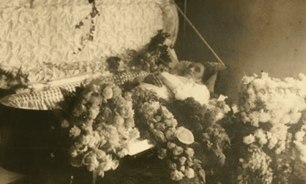 Antique photo of a woman laying in a casket covered in bouquets of flowers
