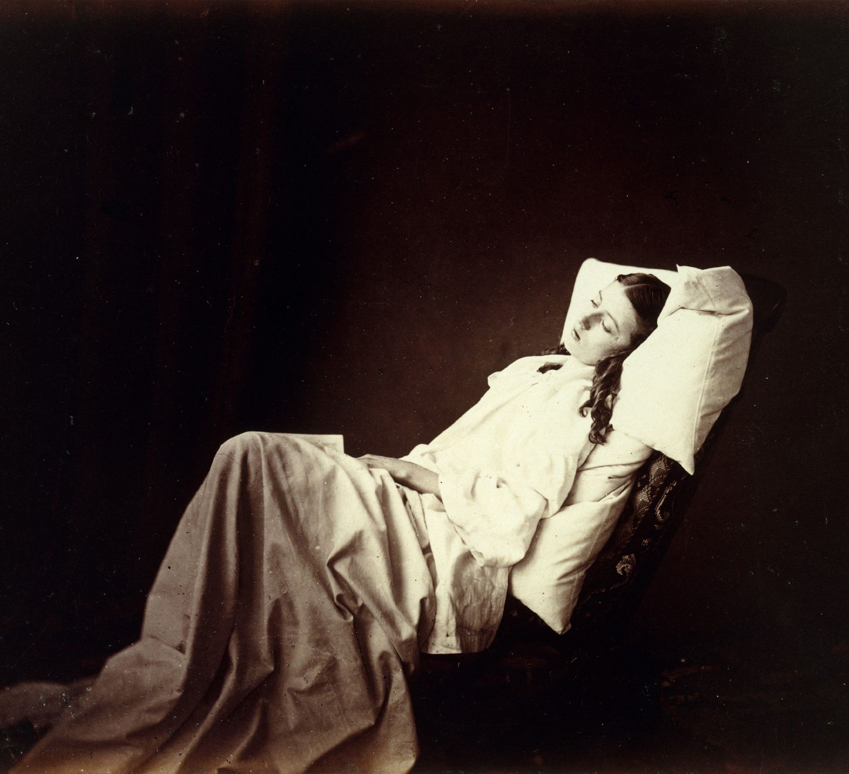 Antique photograph of a woman dressed in white nightgown reclining under a white sheet