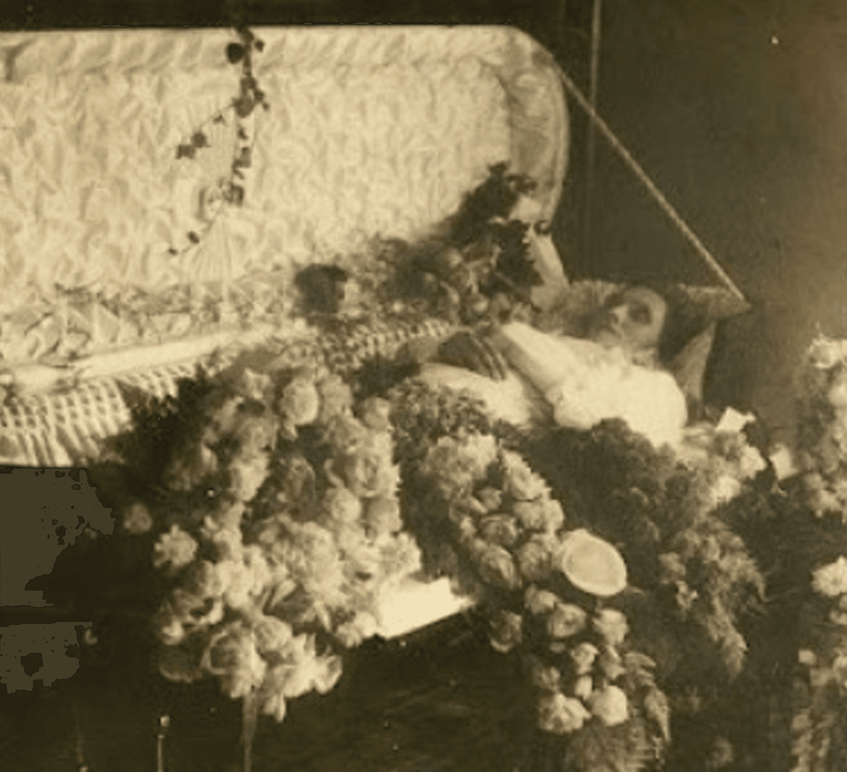 Antique photo of woman lying in casket with elaborate flowers inside and below the casket