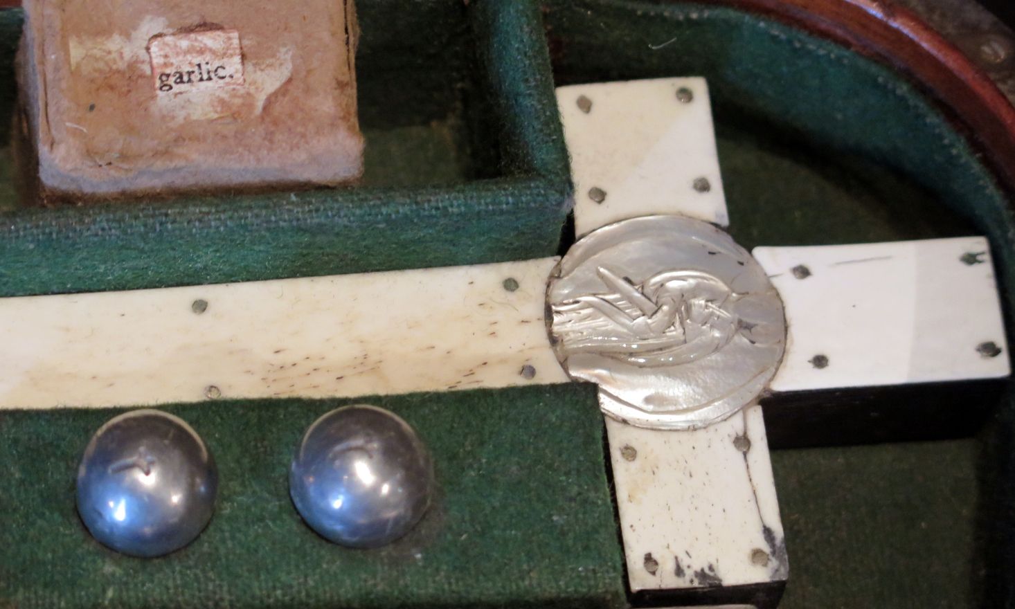 Image of a white cross and a container reading "garlic" in a green fabric lined box