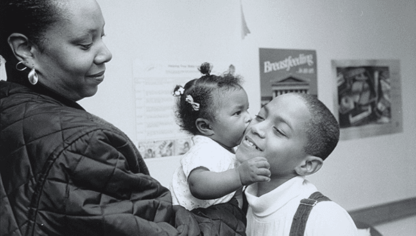 A mother holds a todler n her arms, who kisses an older child on the cheek.