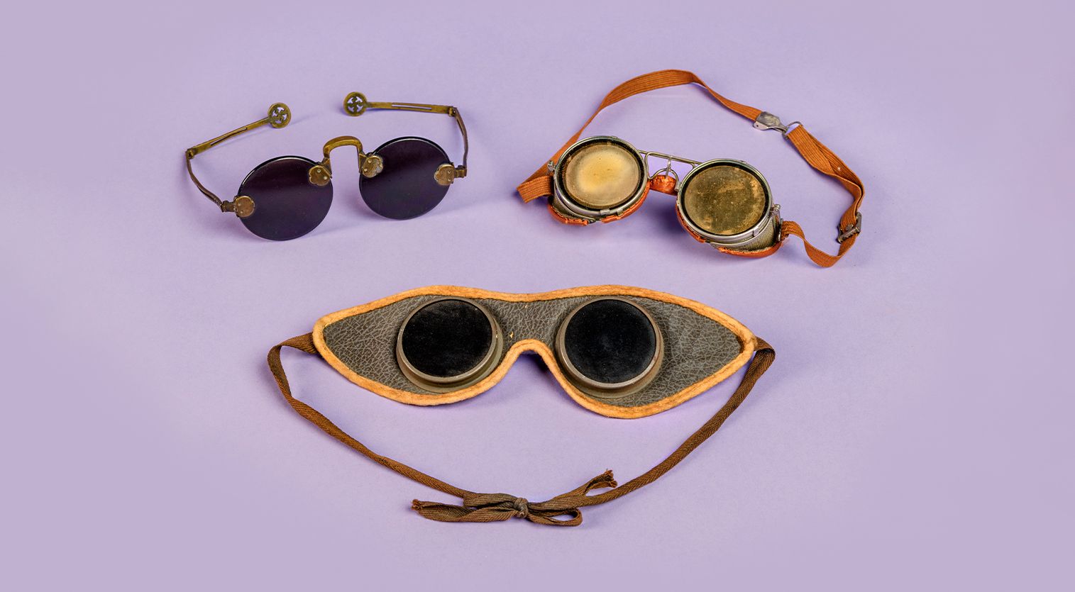 Three different pairs of antique goggles against a purple background