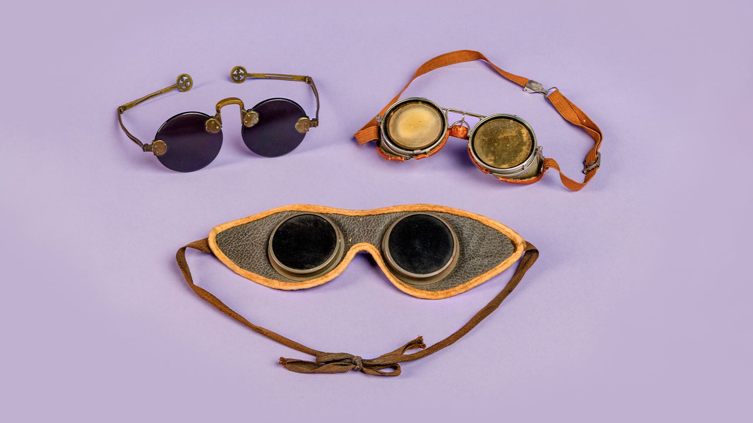 Three different pairs of antique goggles against a purple background