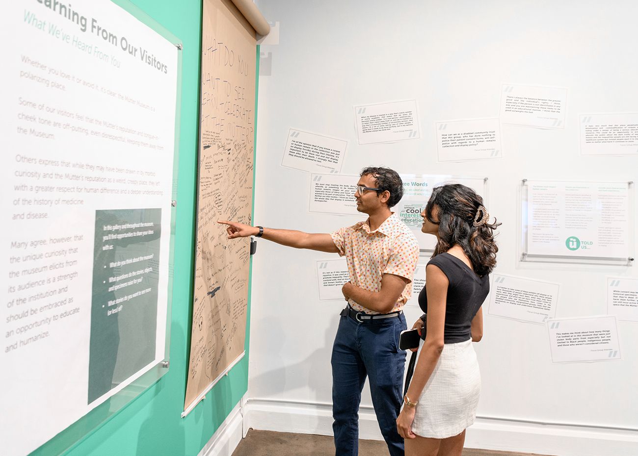 Two people pointing to a piece of butcher paper hanging on the wall with quotes written by Museum visitors