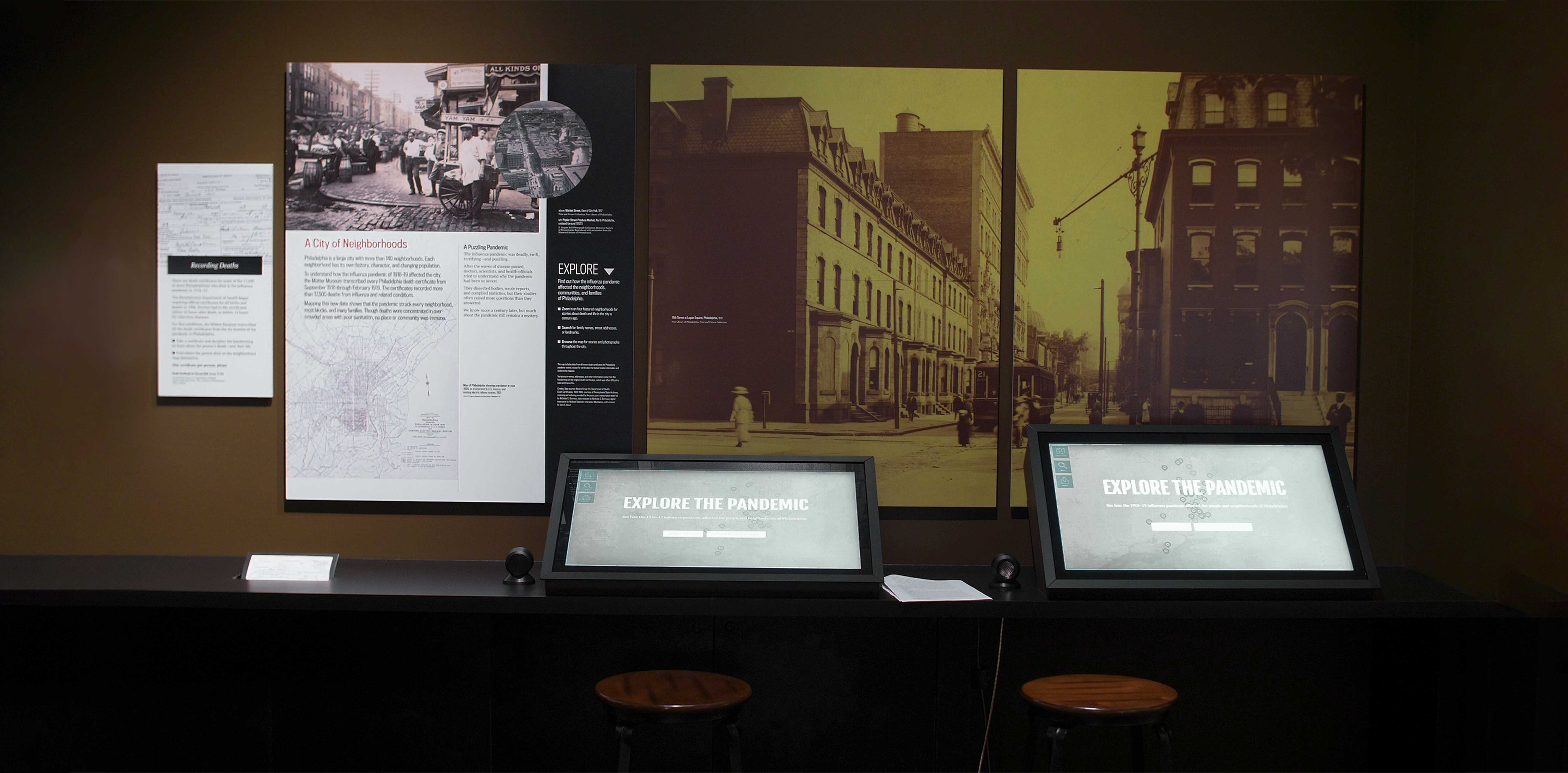 Photo of Spit Spreads Death exhibition with historical photos on the wall and interactive computers that say "Explore the pandemic"