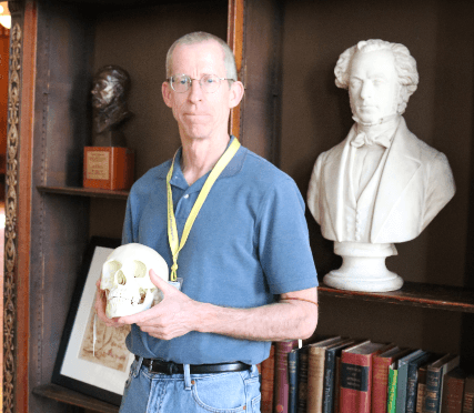 Photograph of Mütter Museum docent Joe Walsh holding a skull next to a bust of Thomas Dent Mütter