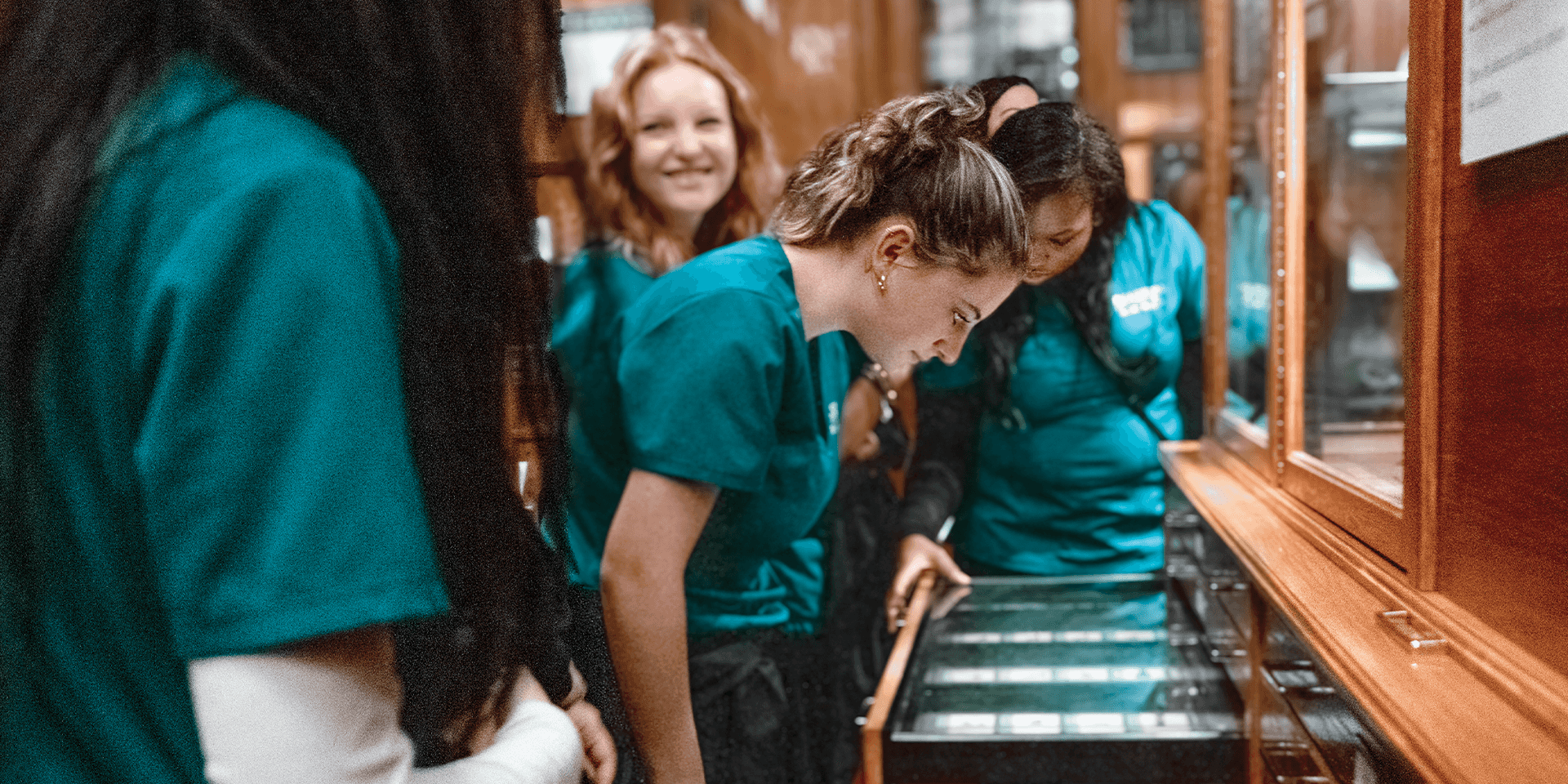 Group of guests in teal scrubs huddled around an outstretched drawer in the Museum gallery