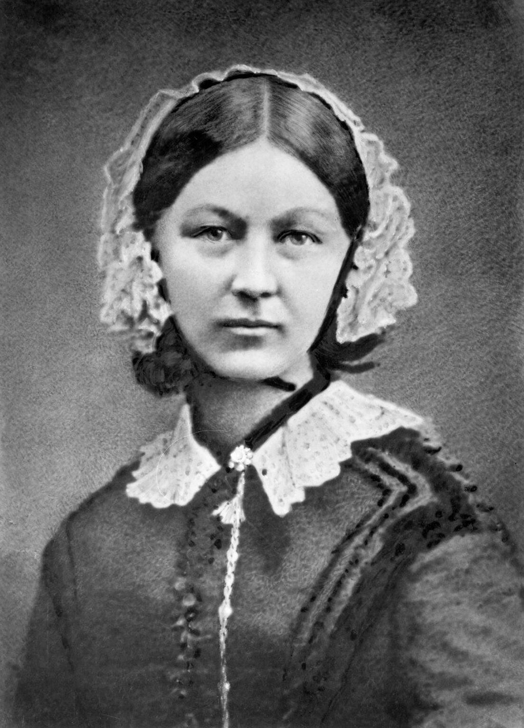 Black and white photo of a woman with dark hair and a lace bonnet, a dark dress, and a lace collar