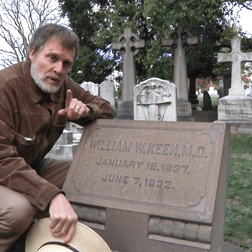 Man kneeling next to a gravestone that reads "William W. Keen, M.D."